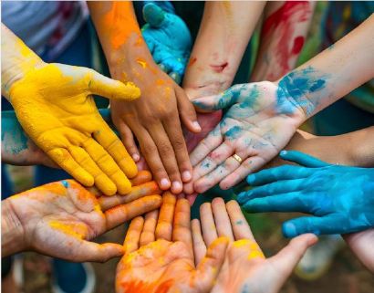 Foto von mehreren Händen, bemalt mit gelber, oranger und blauer Farbe, die in der Bildmitte mit offenen Handflächen zusammenliegen.