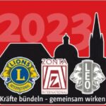 Illustration mit rotem Hintergrund, großer pinker 2023, Stadtsilhouetten und Logos von Lions, Zonta und Leo Club. Text: Kräfte bündeln - gemeinsam wirken.