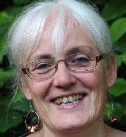 Foto von einer älteren Frau mit weißen Haaren, Brille und Ohrringen vor grünen Blättern. Sie steht für den Vorstand des SkF Aachen.