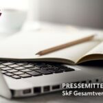 Foto von einem Laptop und einem Notizbuch auf einem Tisch. Beide Gegenstände liegen nebeneinander in einer Arbeitsumgebung.
