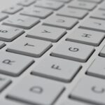 Foto von einer weißen Computertastatur in Nahaufnahme, mit scharfen Buchstaben- und Zahlentasten in diagonaler Anordnung.
